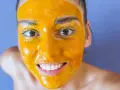 Uśmiechnięta twarz z maseczką z kurkumy na całą skórę. Naturalne piękno i domowe SPA.