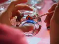 Manos pintando un vaso de cristal con flores de colores. Aprende como pintar cristal a mano y crea arte.