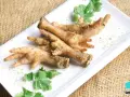 Patas de pollo sazonadas y listas para cocinar, adornadas con cilantro fresco sobre un plato blanco.