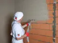Pracownik nakłada tynk maszynowy na ścianę z cegły. Sprawdź atrakcyjną tynki maszynowe cenę!