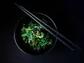 Salade de wakame algue, garnie de graines de sésame, dans un bol noir avec des baguettes.