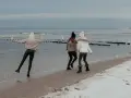 Trzy dziewczyny cieszą się zimowym dniem, gdzie zimą nad morze. Spacerują po plaży, na której leży śnieg, a fale delikatnie rozbijają się o brzeg.