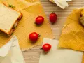 Un sandwich, des tomates et un morceau de fromage sont présentés sur des bee wraps maison à pois rouges sur fond de bois.