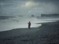 Para spaceruje po czarnej plaży Islandii, podczas gdy fale rozbijają się o brzeg.