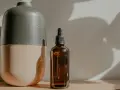 Brązowa buteleczka z pipetką, idealna do aplikacji olej rycynowy na włosy. Obok stoi dwukolorowy, matowy wazon.