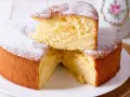Una soffice torta fredda allo yogurt, spolverata di zucchero a velo, con una fetta sollevata che ne rivela la morbidezza.