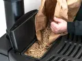 Persona rellena un compartimento de estufa de pellets. Considera el instalar estufa pellets precio para un hogar eficiente.