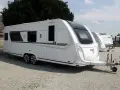 Biała przyczepa kempingowa Knaus Sudwind z przyciemnianymi oknami, zaparkowana na żwirowisku.