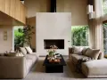 Salón de estilo japandi con sofás beige, chimenea de ladrillo blanco y mucha luz natural.