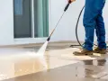 Un homme nettoie sa terrasse carrelage avec un nettoyeur haute pression. L'eau projetée fait briller le sol.