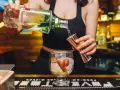 Barman nalewa alkohol z butelki do miarki nad kieliszkiem z lodem i owocami.