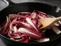 Fette di radicchio rosso vengono saltate in padella con un cucchiaio di legno.