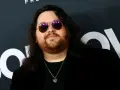 Wolfgang Van Halen w okularach przeciwsłonecznych i z naszyjnikiem w kształcie serca, na tle logo HBO.