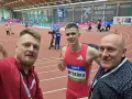 Trzej mężczyźni na bieżni lekkoatletycznej. W środku zawodnik Maciej Wyderka w stroju sportowym.