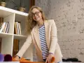Uśmiechnięta kobieta w beżowej marynarce i pasiastym T-shircie, z okularami na nosie. Jej strój to przykład profesjonalnego dress code nauczyciela.