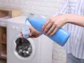 Ręce nalewają niebieski płyn do nakrętki, by wyprać ubrania. To prosty sposób, jak rozmagnesowac ubranie.