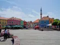 Kolorowy plac w **Tuzla, Bośnia**, z kawiarniami, fontanną i minaretem w tle.