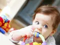 Bébé curieux mordillant un jouet coloré, dans le cadre d'un projet d'accueil individualisé pour son développement.