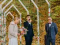 Uroczyste wesele w listopadzie. Panna młoda z bukietem, pan młody przemawia do mikrofonu, a świadek uśmiecha się w tle.