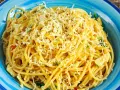 Porcja spaghetti z tartym serem i ziołami w niebieskiej misce.