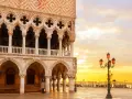 Palazzi storici di Venezia all'alba, con il sole che illumina la piazza e le architetture gotiche.