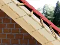 Ocieplenie nakrokwiowe dachu z czerwonej dachówki, widok przekroju z widoczną cegłą i drewnianą konstrukcją.