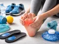 Mani che massaggiano un piede dolente, circondate da attrezzature per la cura dei piedi: scarpe, solette, rulli, palline massaggianti, elastici e impacchi freddi.