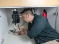 Man with pliers working on a garbage disposal under a sink.