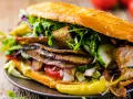 Kebab w bułce z mięsem, warzywami i sosem na drewnianym tle.
