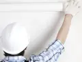 Un ouvrier en casque blanc déroule une **pose toile de verre** sur un mur blanc.