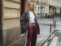 Modella con un outfit vestito con sneakers, blazer grigio, t-shirt bianca e pantaloni bordeaux a righe. Stile sporty chic.