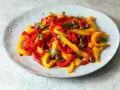 Peperoni in padella, tagliati a listarelle rosse e gialle, conditi con olive e capperi, guarniti con prezzemolo fresco.