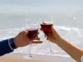 Dwie ręce unoszą kieliszki z czerwonym winem na tle morza. Idealne drinki z winem na romantyczny wieczór.