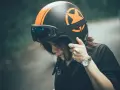 Donna con casco nero e arancione, occhiali riflettenti. Il casco deve calzare bene per la sicurezza.