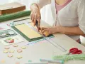 Tworzenie zaproszenia na urodziny: ręce tną papier z linijką, obok ozdoby i nożyczki.