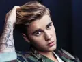 Justin Bieber mit tätowiertem Arm und Camouflage-Jacke, blickt in die Kamera.