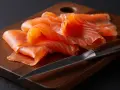 Finas lonchas de salmón ahumado, listas para disfrutar, reposan sobre una tabla de madera junto a un cuchillo.