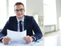 Uśmiechnięty mężczyzna w okularach i garniturze trzyma dokument, wyjaśniając, kredyt inkaso co to jest.