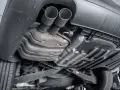 The underside of a car shows a dual exhaust system leading to a large muffler, which is a key component for reducing engine noise.