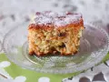 Wilgotne ciasto marchewkowe, posypane cukrem pudrem, na szklanym talerzyku.