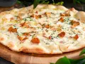 Pyszna pizza z kurkami, polana kremowym sosem i posypana świeżymi ziołami, podana na drewnianej desce.