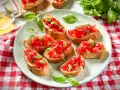 Frische Crostini Variationen mit Tomaten und Basilikum auf einem Teller, garniert mit frischen Basilikumblättern.