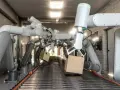 Wiele ramion robotów współpracujących chwyta kartony na linii produkcyjnej.
