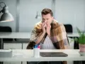 Chory pracownik w biurze, owinięty kocem, dmucha nos w chusteczkę. Czy na wypowiedzeniu można iść na L4?