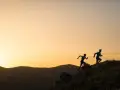 Dos corredores se enfrentan a una exigente carrera de senderos al amanecer, sus siluetas recortadas contra un cielo anaranjado.