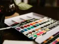Une palette de matériel peinture aquarelle aux couleurs vives, prête à l'emploi. Un pinceau est posé à côté.
