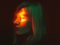 Profilo di donna con luce arancione sull'occhio, evocando un'emicrania oculare. Capelli illuminati da luci verdi e rosse.