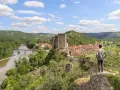 Un homme admire un village médiéval avec un château, un fleuve et des collines verdoyantes, un aperçu du circuit des plus beaux villages du Lot.