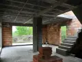 Wnętrze budowy z widocznym stropem gęstożebrowym, schodami, ceglanymi ścianami i otwartymi drzwiami na zewnątrz.