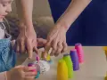 Dziecko i dorosły ćwiczą zdolności manualne, układając kolorowe kubeczki.